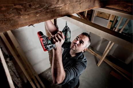 Man using a power drill on wooden beams inside a building.