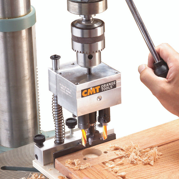 CMT Orange Tools drill press on a wooden surface with a hand operating it.