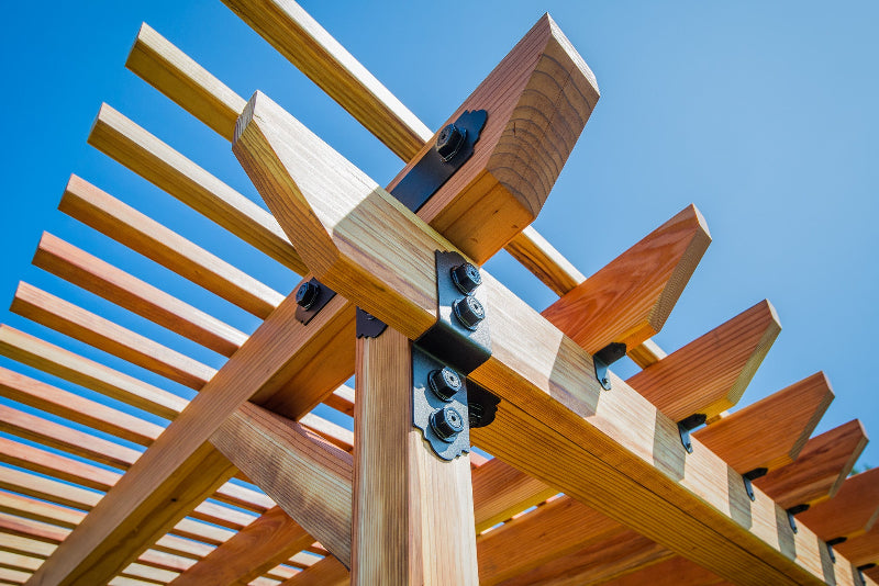 Wooden pergola structure with metal brackets against a clear blue sky