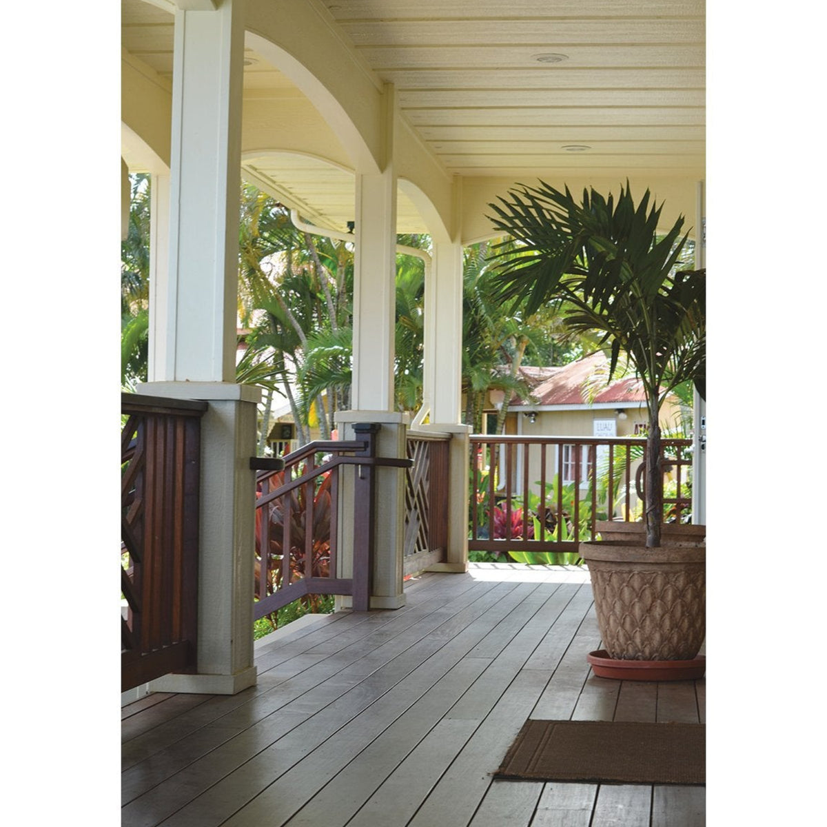 A scenic view of a wooden porch with cream pillars, a dark wood railing, and a large potted palm tree on a light gray background.