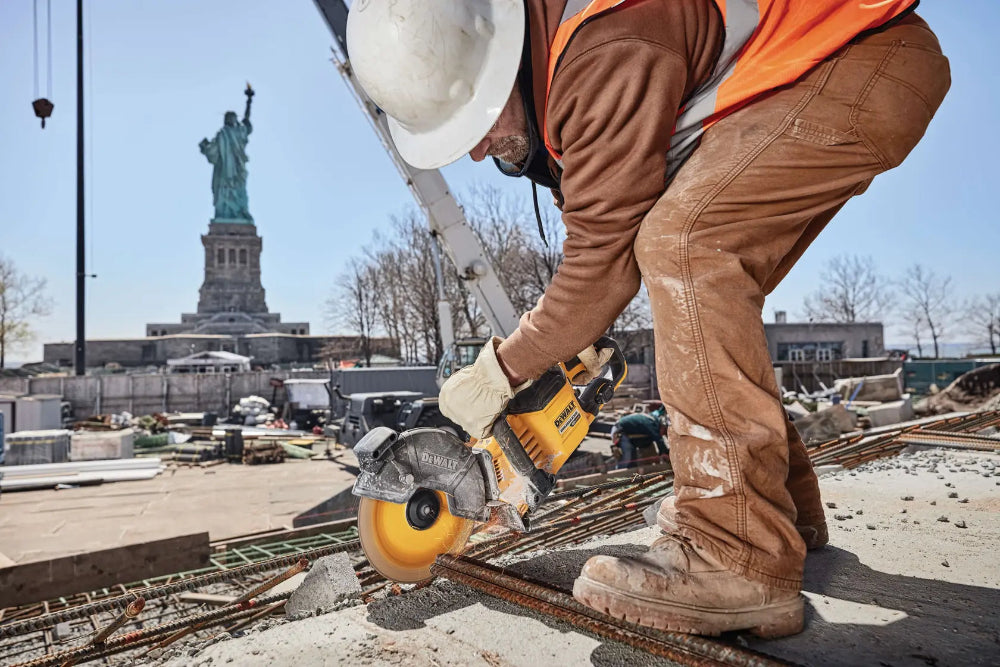Construction worker cutting rebar with a circular saw in front of the Statue of Liberty.