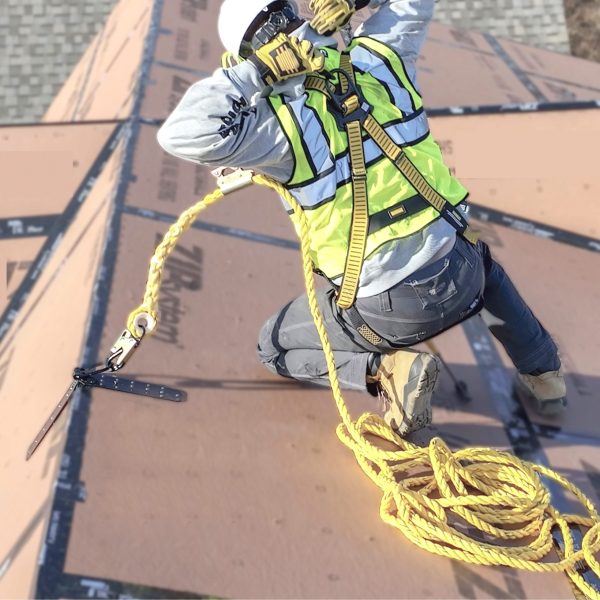 Person on a roof using a safety harness and rope, with construction materials in the background.