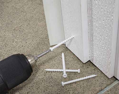 Drill and screws on a concrete floor with a white door frame in the background