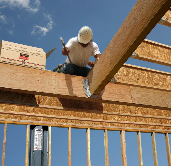 Person working on a wooden structure with tools against a blue sky.