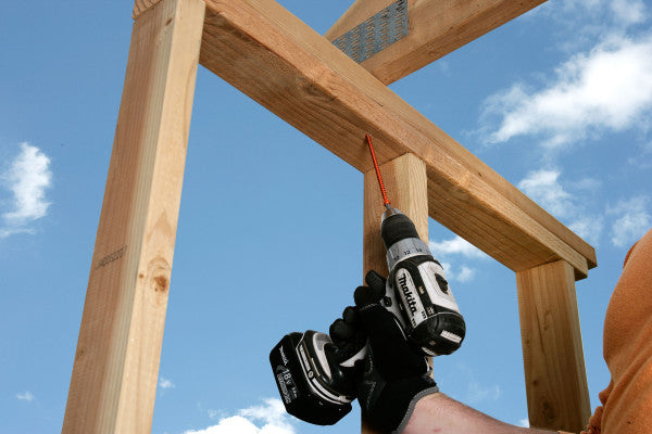 Person using a power drill on wooden beams against a blue sky