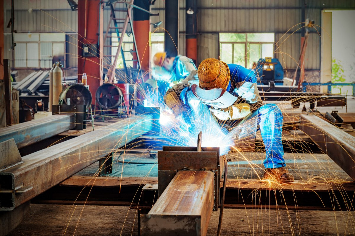 Worker welding metal structures in a factory setting with sparks flying