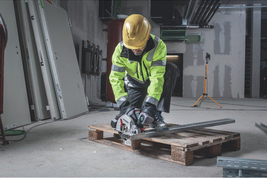 Person in high-visibility jacket and hard hat using a power tool on a wooden pallet.
