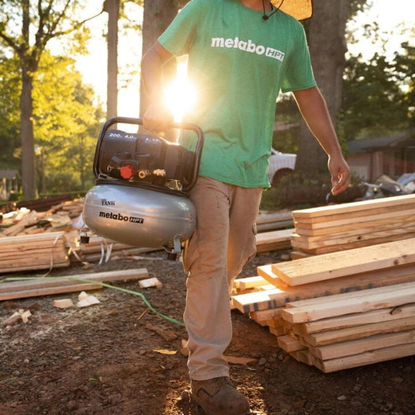 Person wearing a green Metabo HPT shirt carrying a Metabo HPT air compressor on a construction site.